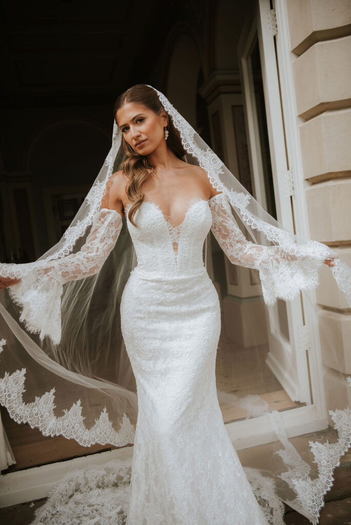 Lyra by Lottie & Meg from Wedding Belles of Four Oaks Chantilly fitted lace Wedding dress with optional sleeves paired with cathedral lace veil
